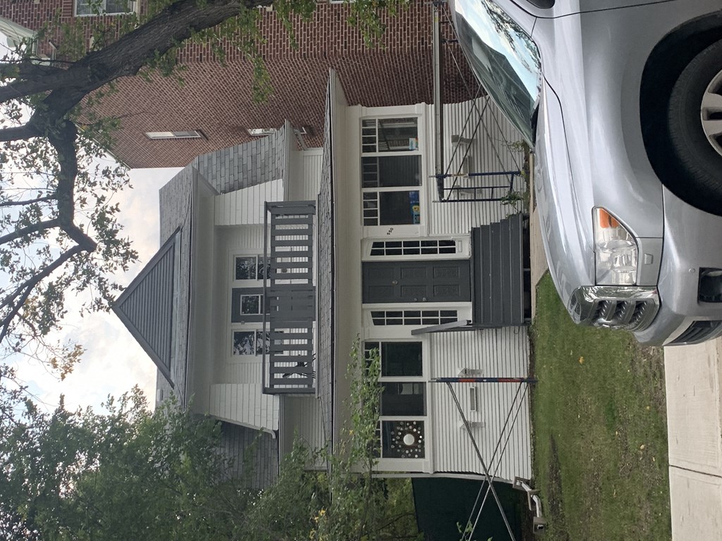 A car is parked in front of a building with a tree in the foreground.