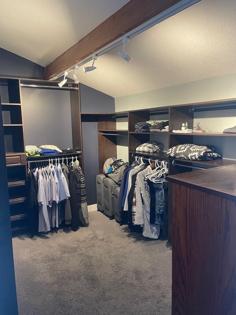 A walk in closet with clothes hanging and shelves.
