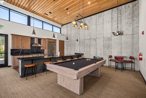 A billiards table is in the middle of a room with a bar and a kitchen.