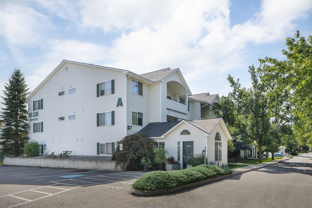 the exterior of a white apartment building with trees and a parking lot