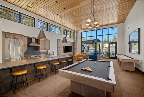 A billiard table is in the middle of a room with a kitchen area and a balcony.
