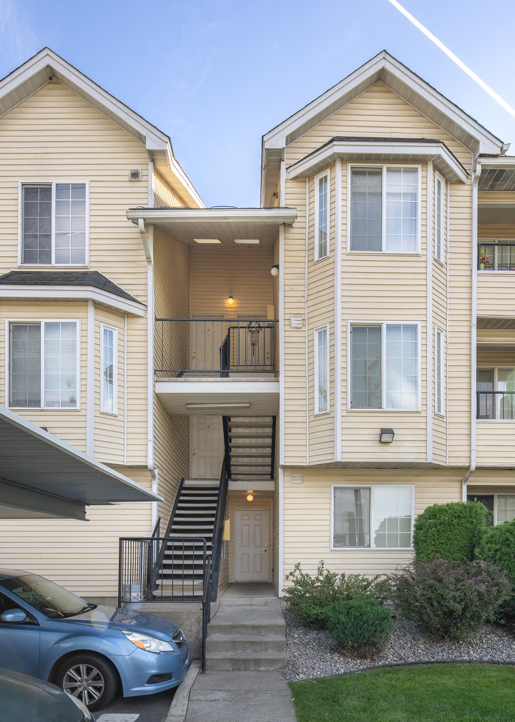 a yellow apartment building with stairs and a blue car parked in front