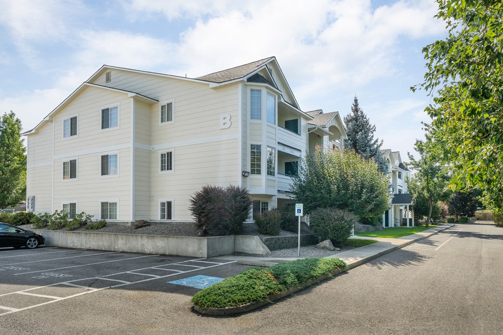 the view of a white apartment building with a parking lot