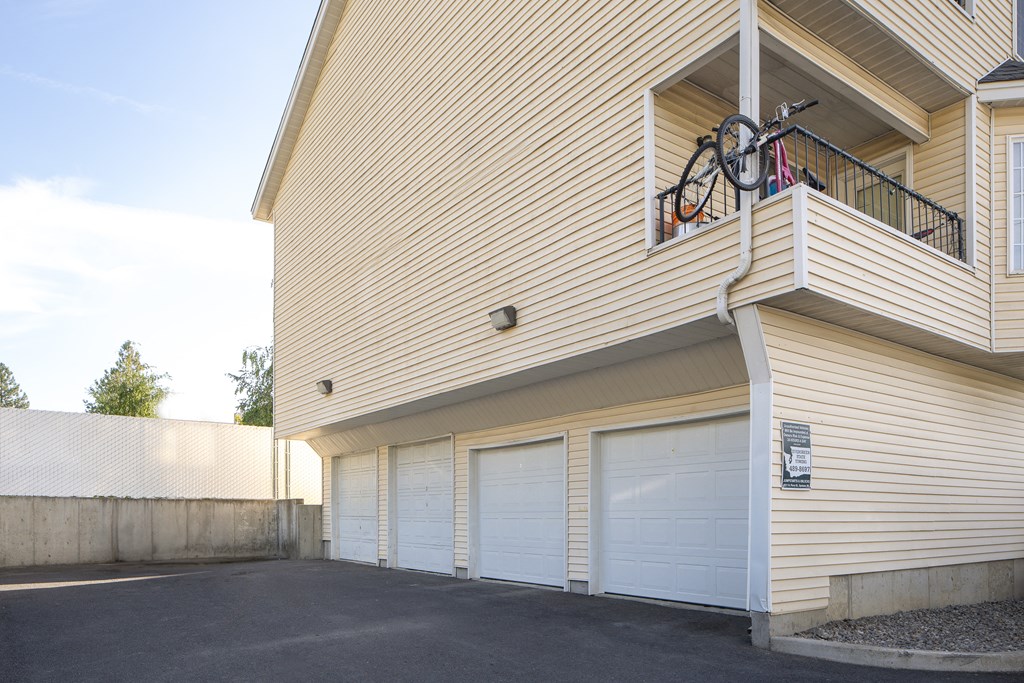 the side of a building with white garage doors and a bike on the balcony