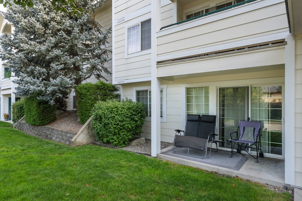 a patio with two chairs and a tree in front of a white house
