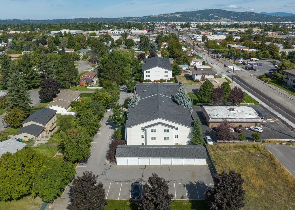 an aerial view of a white building with a gray roof and a street and trees