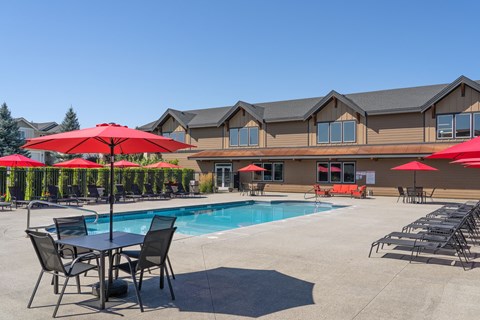 A pool area with red umbrellas and chairs in front of a building.