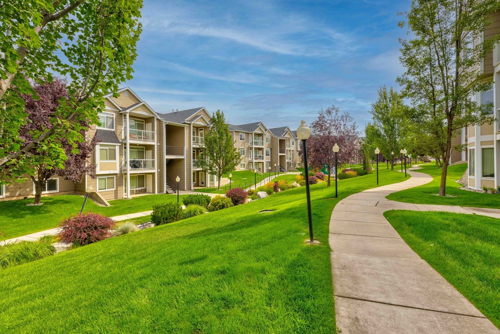 a sidewalk leading to an apartment complex with green grass and trees