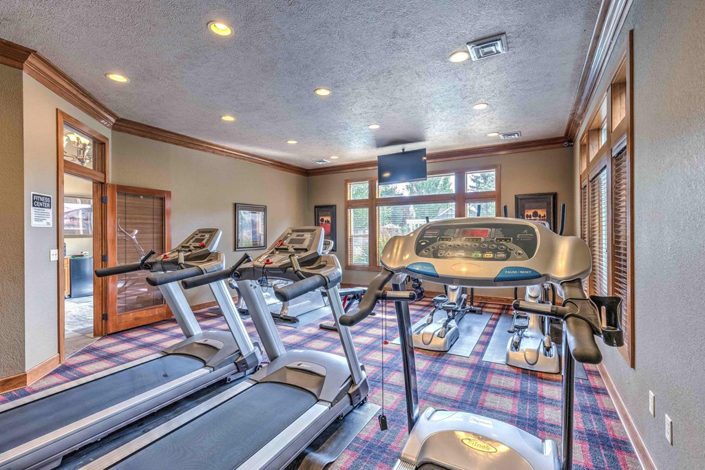 a gym with treadmills and weights in the corner of a room with windows