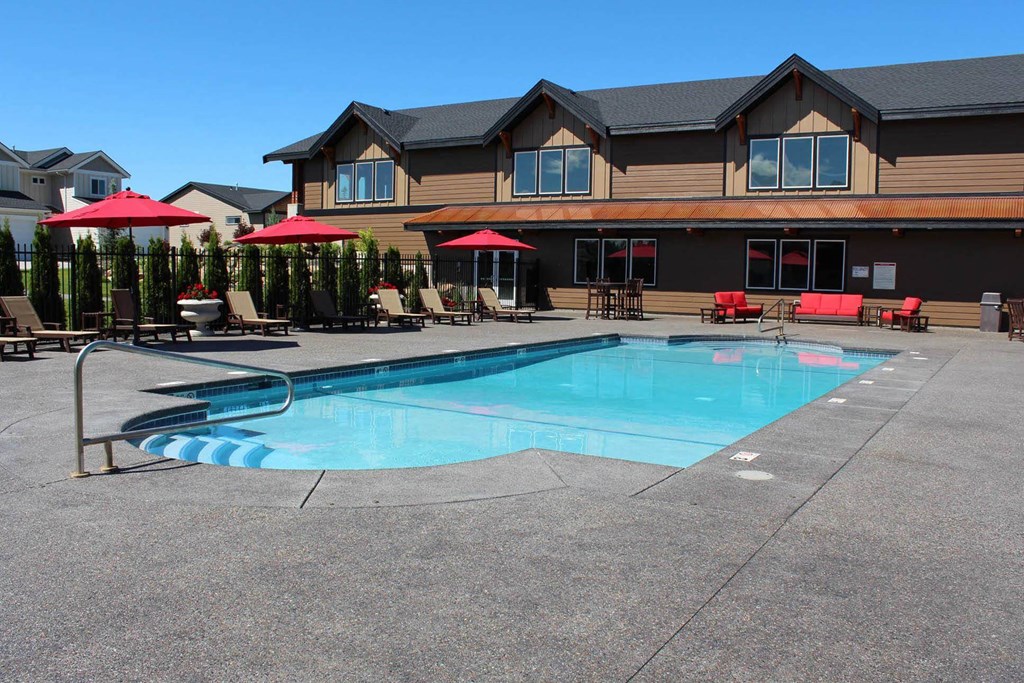 a swimming pool in front of a hotel with chairs and umbrellas