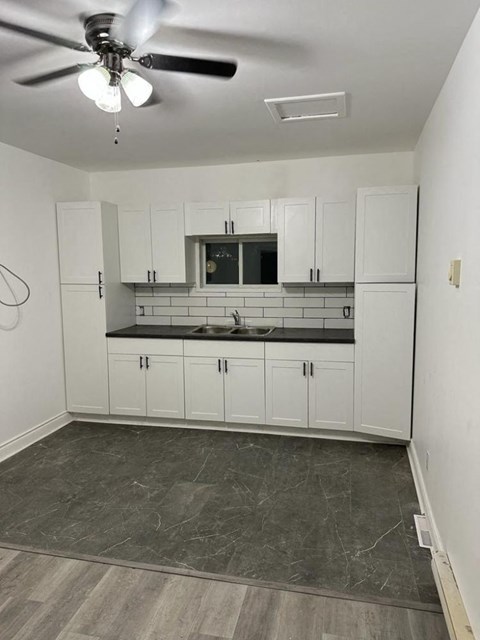 an empty kitchen with white cabinets and a ceiling fan