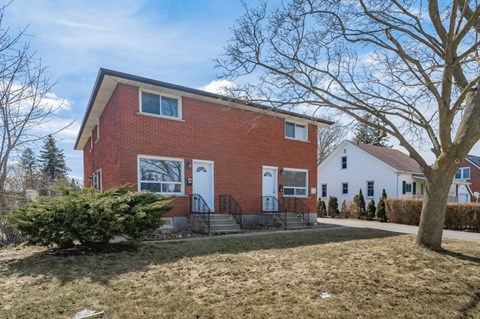 the front of a brick house with a yard and a tree