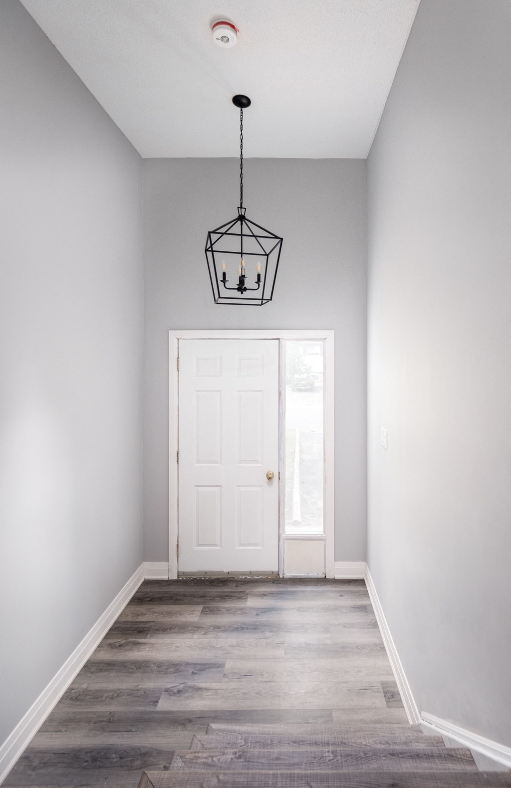 an empty hallway with a white door and a chandelier