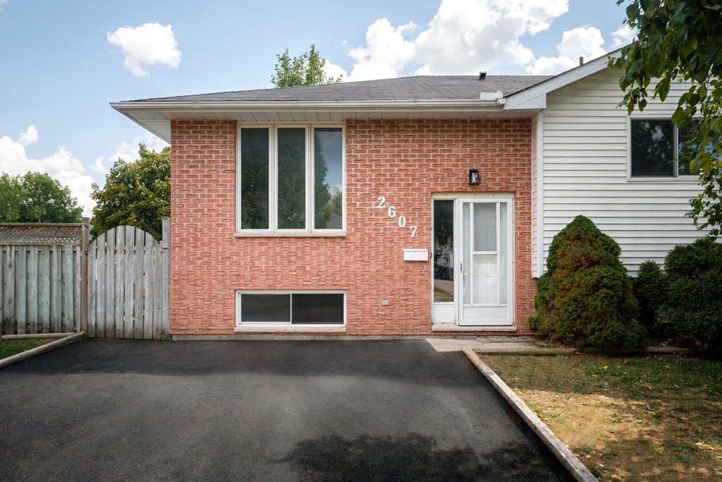 the front of a brick house with a driveway and a white fence