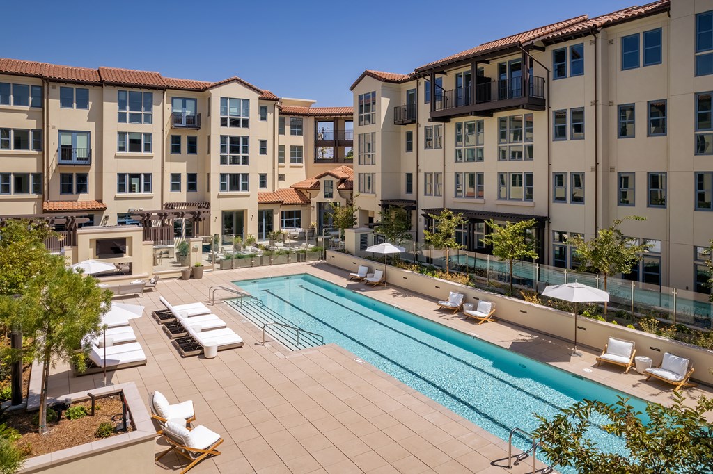 long pool with lounge chairs and hot tub to the side surrounded by apartments