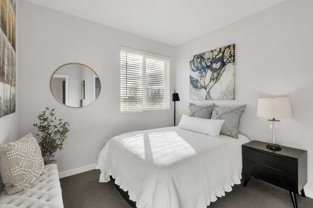 A bedroom with a large bed, a round mirror, and a painting on the wall.