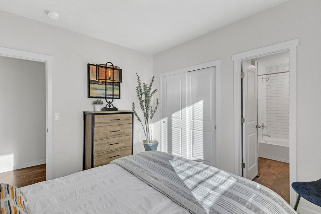 A bedroom with a bed, dresser, and a window with blinds.