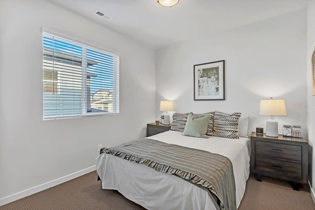 A bedroom with a bed, nightstands, and a window with blinds.