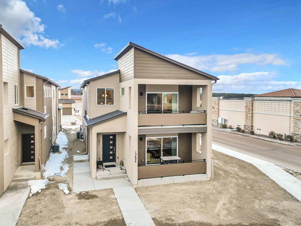 A modern house with a brown roof and beige walls is surrounded by other similar houses.