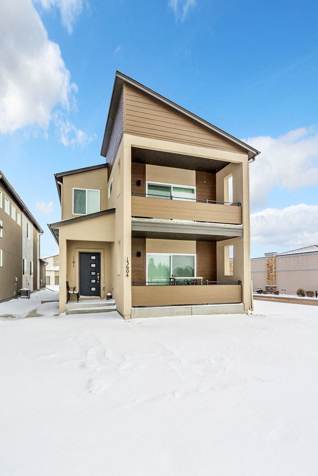 A modern house with a black door and windows is surrounded by a snowy landscape.