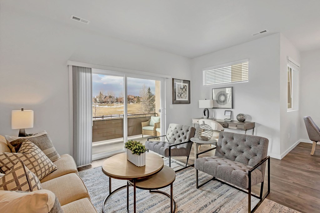 A living room with a grey sofa, a round table, and a large window with a view of the outside.