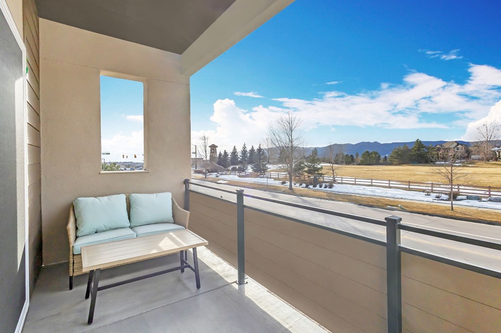 A balcony with a bench and a view of the street and trees.