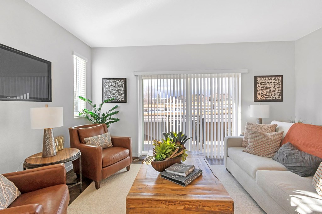 A living room with a brown leather couch, a white sofa, a wooden coffee table, and a flat-screen TV mounted on the wall.
