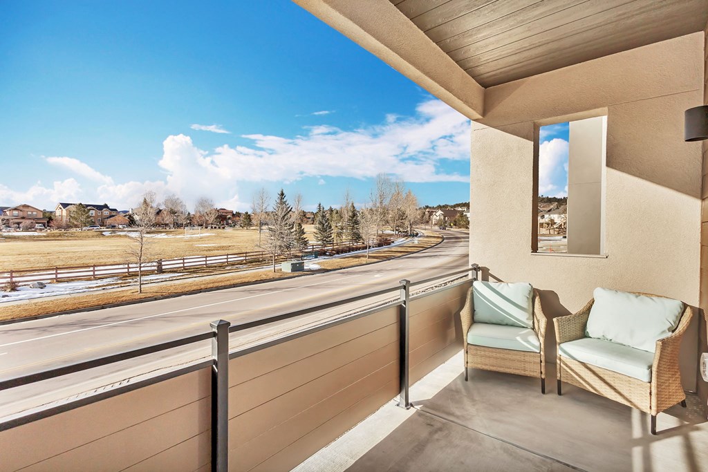 A balcony with two chairs and a table overlooking a road.