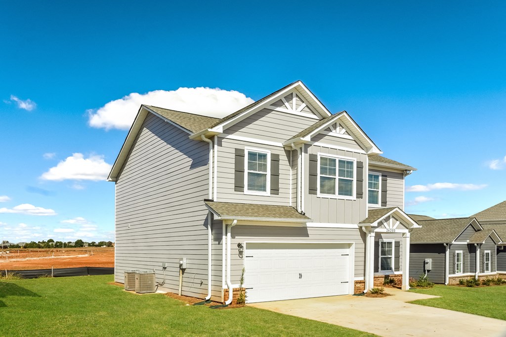 a gray house with white siding and a field in the background