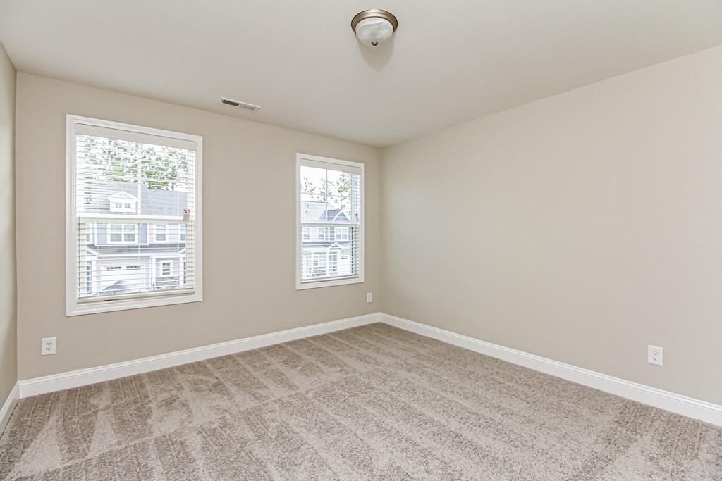 an empty living room with carpet and two windows