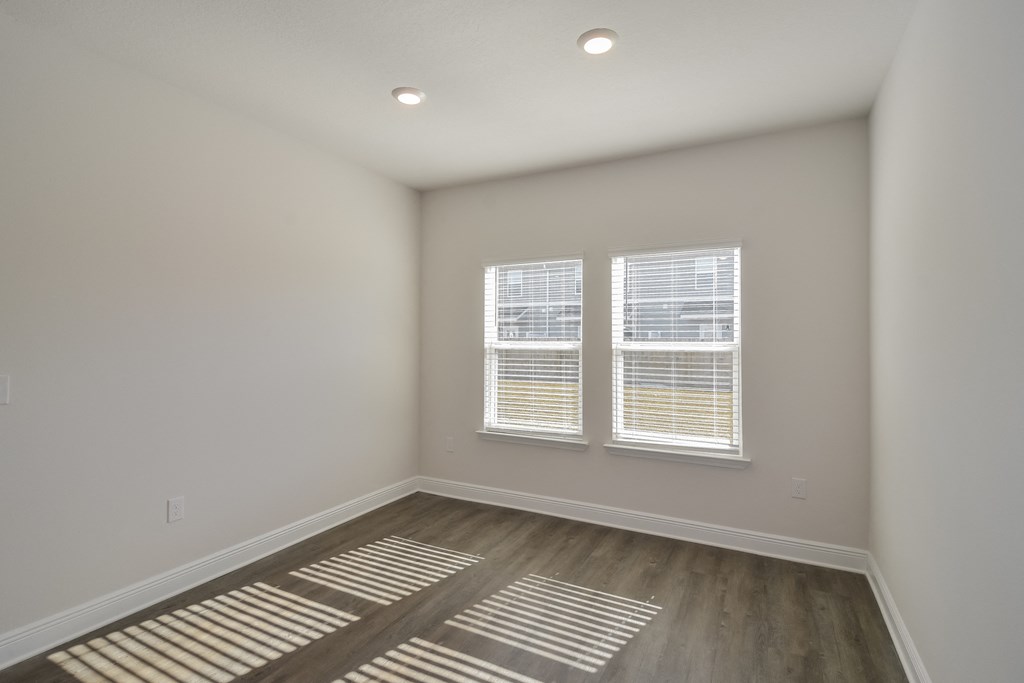an empty room with wooden floors and two windows