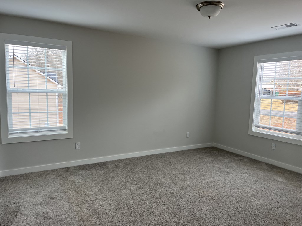 an empty living room with two windows and a carpet