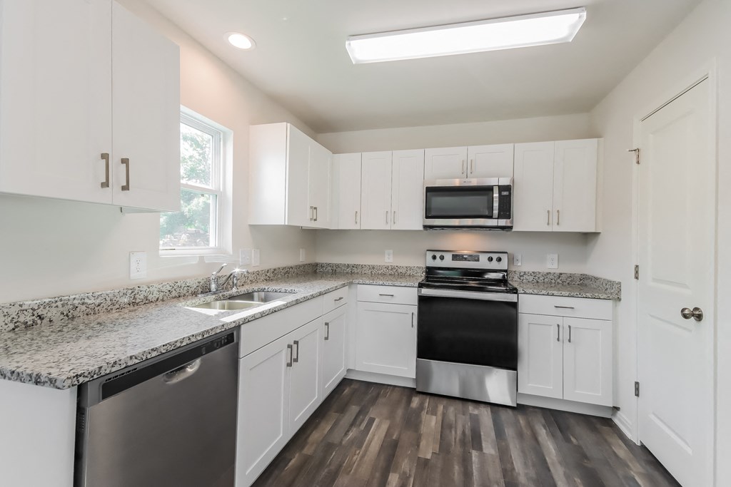 an empty kitchen with white cabinets and granite counter tops and a black stove and microwave