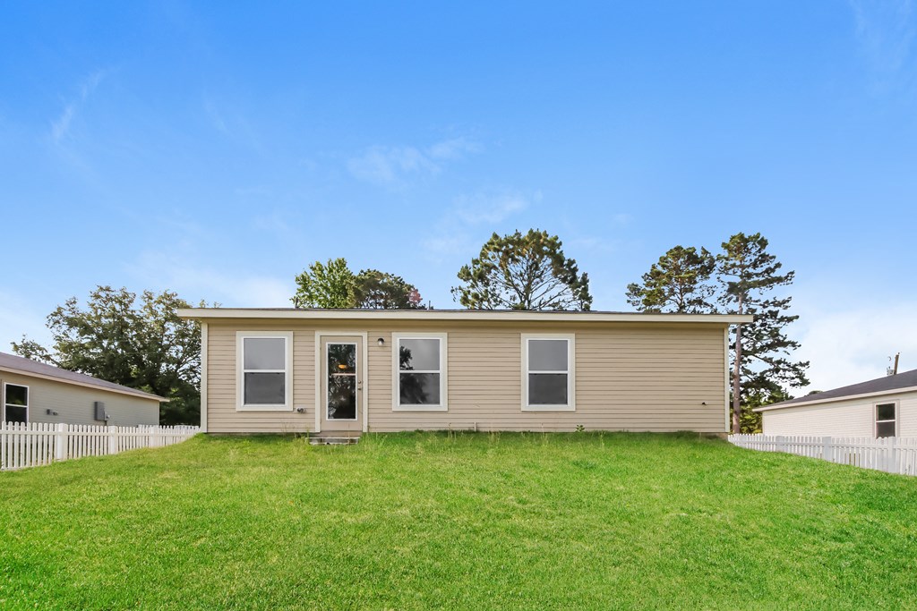 a tan house on a grassy hill with trees in the background