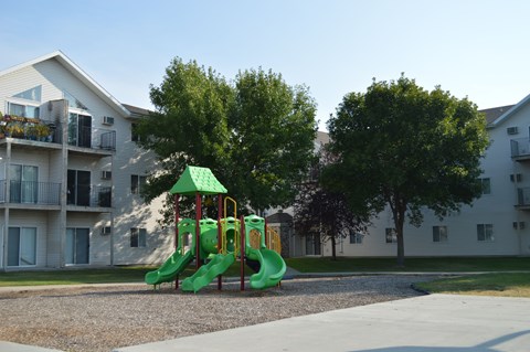 A playground with a green slide in front of apartment buildings.