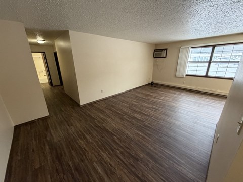 A room with wooden flooring and a window with white curtains.