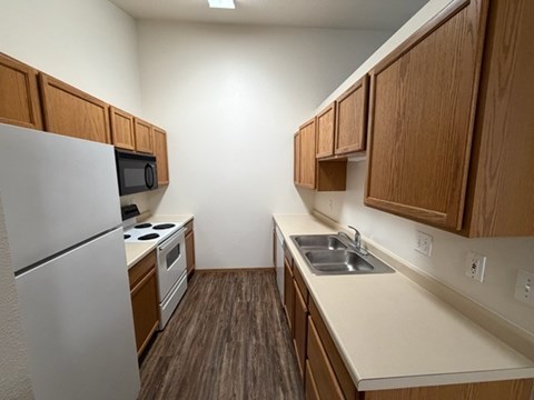 A kitchen with a refrigerator, microwave, oven, sink and cabinets.