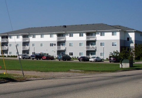 A large white apartment building with a parking lot in front.