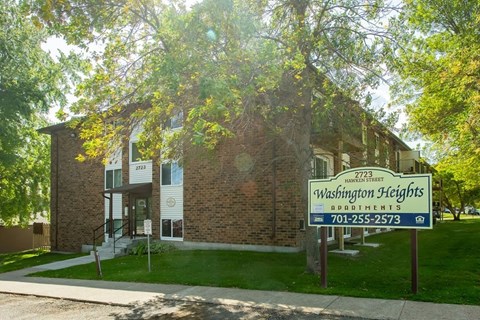 A sign for Washington Heights Apartments is in front of a brick building.