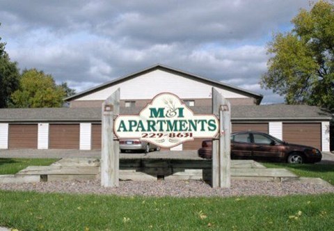 A sign for M&I Apartments stands in front of a building.