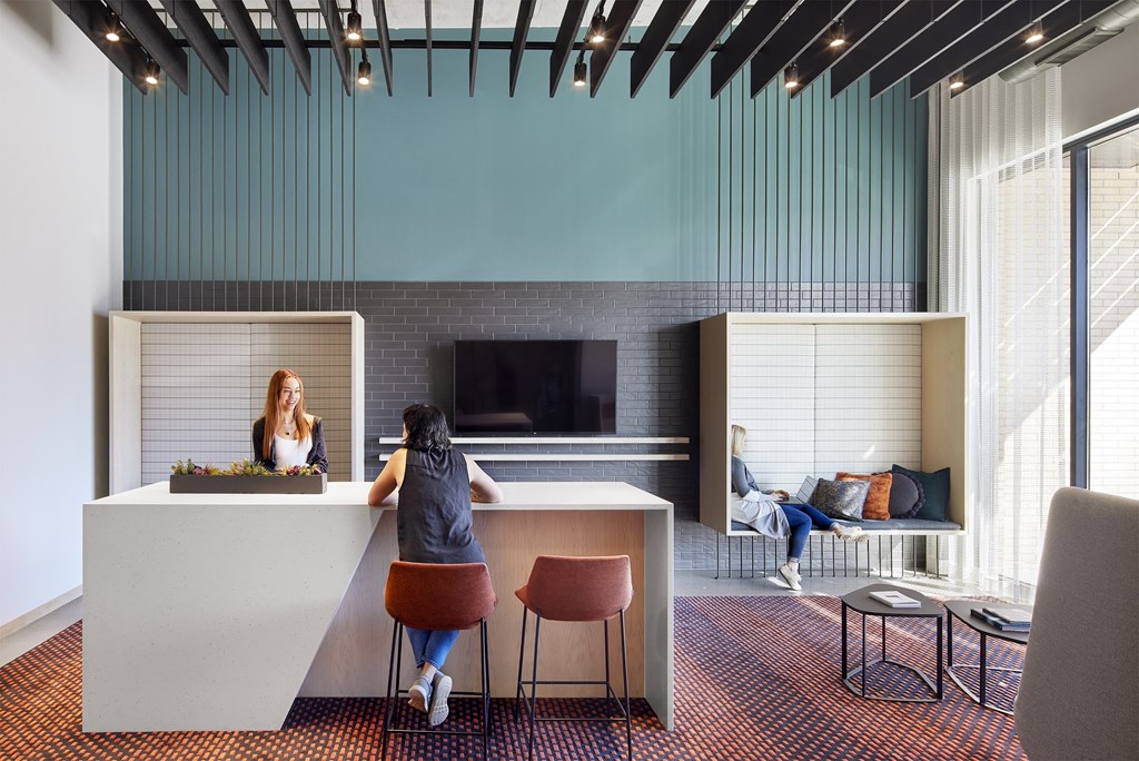 two women sit at a desk in a room with a large window