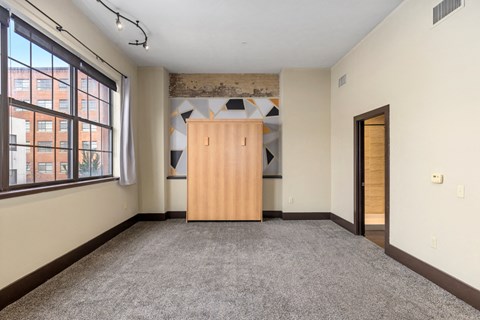 A room with a wooden wardrobe and a window overlooking a building.