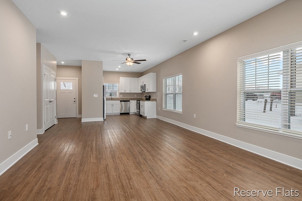 an empty living room with a kitchen and a ceiling fan