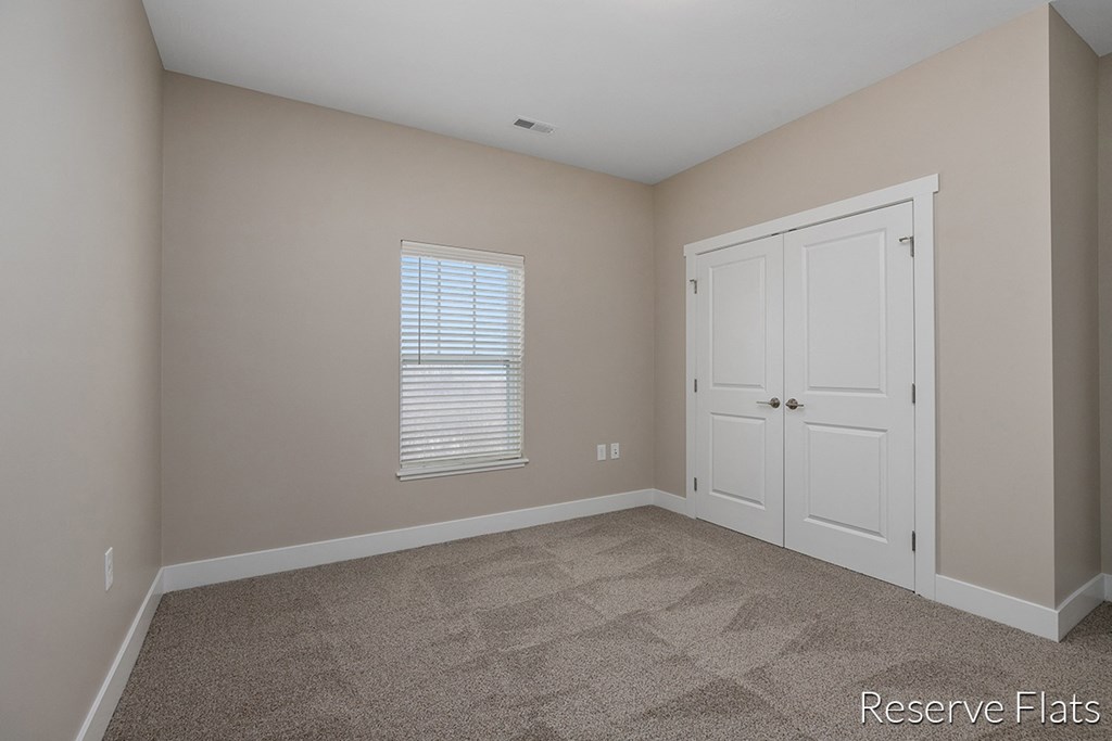 a bedroom with carpet and a white door and a window