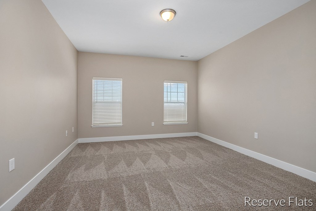 an empty room with carpet and two windows