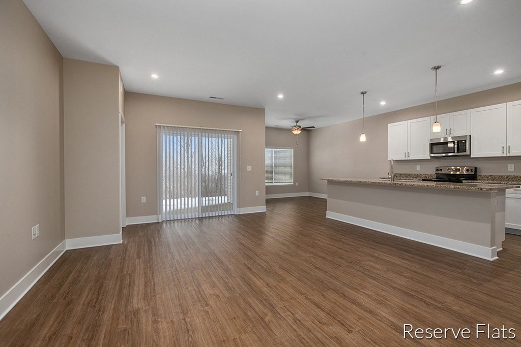 an empty living room with a kitchen and a large window