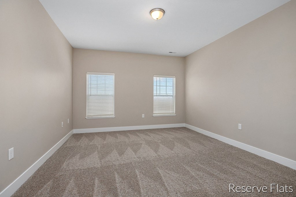 an empty room with carpet and two windows