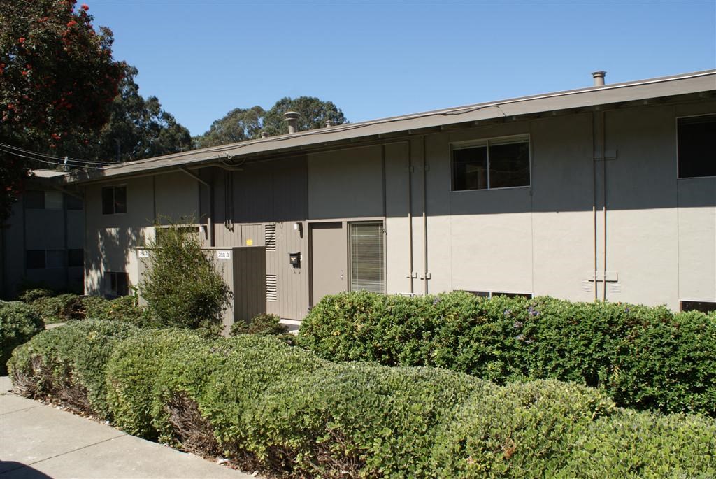 a white building with a sidewalk and hedges in front of it