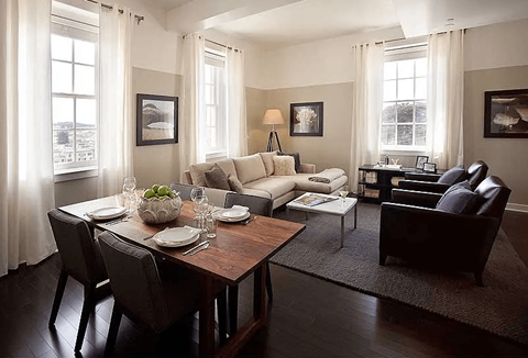 A dining room with a table set for two and a couch in the background.