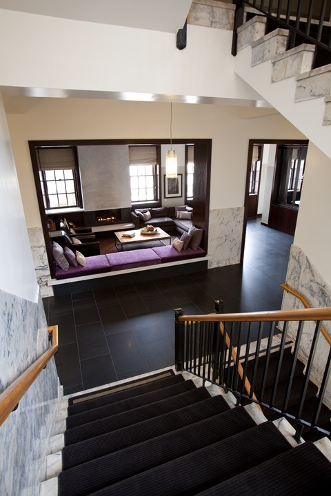 A staircase with a black carpeted runner leads to a living room with a couch and a coffee table.